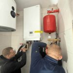 Dwóch techników podczas montażu hydraulicznego pompy ciepła Rotenso i naczynia przeponowego w Radomiu.